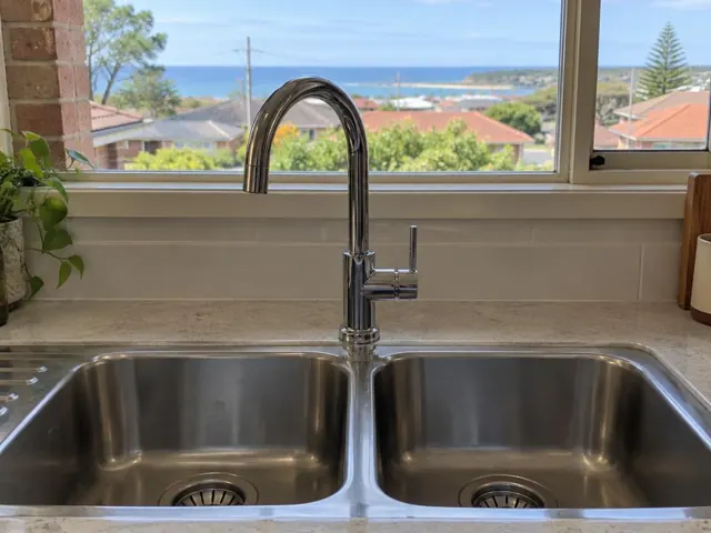 Chrome kitchen mixer tap over a stainless double sink beneath a window in a light tiled kitchen in Bar Beach